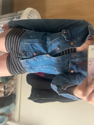 Blå klassisk jeansjacka - Säljer en blå jeansjacka med snygga kopparfärgade knappar och klassiska fickor på bröstet. Jackan har en tidlös design med raka linjer och är perfekt att slänga på över en t-shirt. Passar dig som gillar en avslappnad och cool stil.
