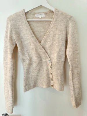 Beige omlottkofta från Gina Tricot - Mysig beige omlottkofta från Gina Tricot med v-ringning och långa ärmar. Koftan har en figurnära passform. 💕💕