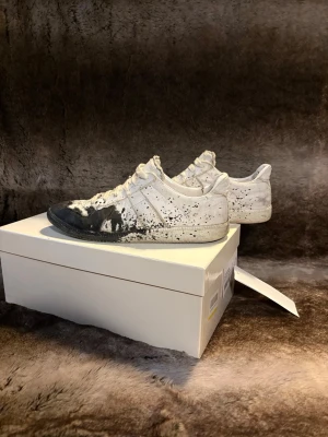 Maison margiela gats - Tjena, säljer nu mina maison margiela gats, med svart färg stänk. Jag har lämnat in skorna då det innan har varit ett litet hål i sulan samt vid hälen, men det är nu löst och dem är stabila. Allt orginal medföljer. Skorna är äkta och riktigt snygga och bra till sommaren! Hör av er vid funderingar!