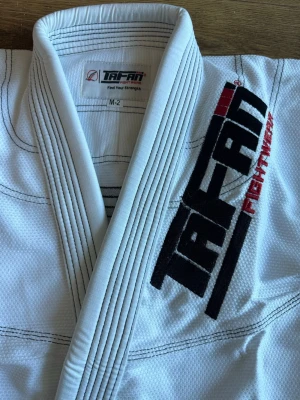 Kids Vit BJJ gi från TAFAN Fightwear M2 - Säljer en vit brasiliansk jiu-jitsu gi från TAFAN Fightwear. Dräkten har förstärkta sömmar, svart och röd logga på jackan samt elastisk midja på byxorna. Materialet är slitstarkt och andas bra, perfekt för träning och tävling.
