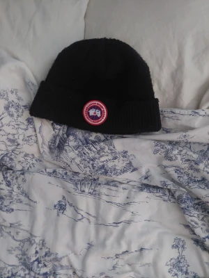 Canada Goose mössa ÄKTA priset kan pratas - Säljer en svart ribbstickad mössa från Canada Goose med klassisk rund logotyp framtill. Mössan har uppvikt kant och är tillverkad i ett mjukt, värmande material som passar perfekt för kyliga dagar.