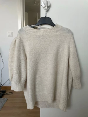 Krämvit stickad tröja med puffärm - Mysig krämvit stickad tröja med puffärmar och bred ribbad kant vid hals, ärmslut och nederkant. Från VeroModa💞