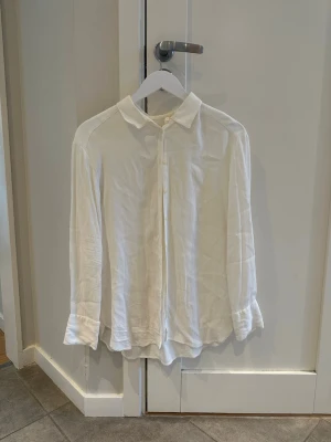 Vit klassisk skjorta från Boomerang - Säljer en stilren vit skjorta från Boomerang i klassisk modell. Skjortan har långa ärmar, knappar framtill och en mjuk krage. Perfekt till både jeans och kostymbyxor. Tillverkad i ett tunt och skönt material som känns lyxigt mot huden.