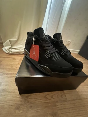 Svarta Air Jordan 4 Retro sneakers - Säljer ett par svarta Air Jordan 4 Retro sneakers med klassisk Jumpman-logga på plösen. Skorna har meshdetaljer, svarta skosnören och en robust sula. Materialet är en mix av mocka och syntet. Perfekta för dig som gillar streetwear och ikoniska modeller.