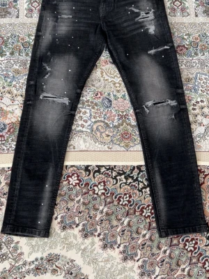 Svarta distressed jeans Supply & Demand - Säljer ett par svarta jeans från Supply & Demand med slitningar och distressed detaljer. Jeansen har skinny fit, coola rivna partier och små vita stänk för en trendig look. Perfekta för dig som gillar streetstyle och vill sticka ut.