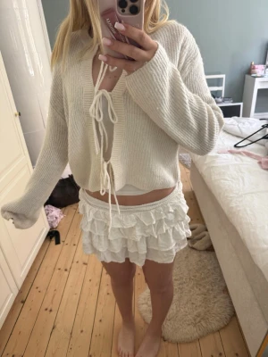 Vit stickad kofta med knytband - Säljer en söt vit stickad kofta med långa ärmar och knytband. Perfekt för våren och sena sommar kvällar. Säljer pga tycker inte den sitter fint på mig. Den har ett litet hål vid nacken men det skyns inte mycket.