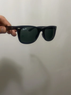 Svarta Ray-Ban Wayfarer solglasögon - Säljer ett par klassiska Ray-Ban Wayfarer solglasögon med svart plastbåge och mörka linser. Ikonisk design med Ray-Ban-logga på linsen och sidan. Perfekt för dig som vill ha en tidlös och cool look.