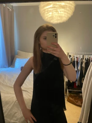 Svart ärmlös halterneck topp - Snygg svart ärmlös topp med halterneck-modell. Toppen har en clean och stilren look som passar perfekt till jeans eller kjol. Materialet känns mjukt och följsamt mot kroppen och ger en modern vibe.
