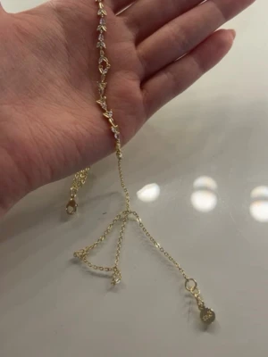 Guldigt halsband från SNÖ - Ett elegant guldigt halsband från SNÖ med små vita pärlor och detaljerade länkar. Halsbandet har en tunn kedja och ett hjärtformat märke med SNÖ-loggan. Perfekt för att ge din look en extra touch av stil.