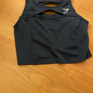 Marinblå sporttopp från Gymshark - Säljer en marinblå sporttopp från Gymshark med ett stilrent snitt och öppna detaljer på ryggen. Perfekt för träning och ger bra stöd. Toppen är ärmlös och tillverkad i ett stretchigt material för optimal rörelsefrihet.