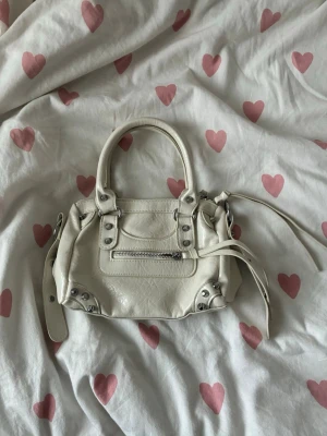 Stockholmstil väska - Säljer en härlig benvit liten väska med silverdetaljer. En längre rem kan också medfölja. Utmärkt skick. Jag köpte från Vinted, men köpte förmodligen från utlandet ursprungligen. Påminner mig om Balenciagas Citybag🤍