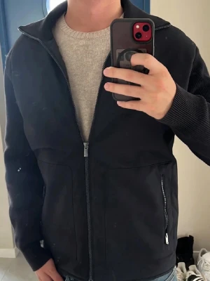 Massimo Dutti Cardigan  - Säljer en Massimo dutti jacka med dragkedja och stickade ärmar. Jackan har två fickor med dragkedja och en hög krage. Perfekt för dig som vill ha en stilren och enkel look. Materialet är blandat tyg och stickat, vilket ger en skön känsla.