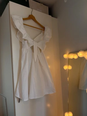 Vit kortklänning med volang och knyt, studentklänning  - Superfin vit kortklänning med breda volangärmar och snygg knytning baktill. Klänningen har en luftig passform och djup v-ringning, delvis öppen rygg: perfekt för studenten!Materialet känns lätt och bekvämt mot huden. Jag brukar ha mellan S och M i storlek och på mig satt dem perfekt! Säljer pga redan har en studentoutfit🙃Köpt här på Plick för 700, pris går att diskutera
