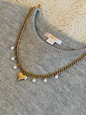 Guldigt halsband med pärlor och hjärta - Säljer ett chunky guldigt halsband rostfritt med vita pärlor och ett stort hjärtformat hänge. Kedjan är kraftig och har en cool vibe som verkligen sticker ut. Perfekt för dig som gillar statement-smycken och vill ha något unikt.