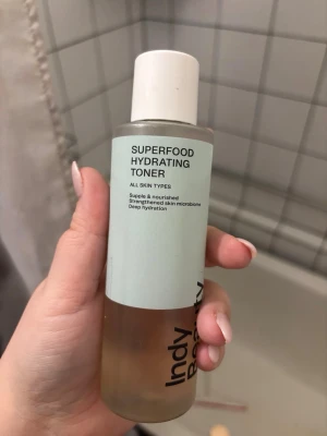 Superfood Hydrating Toner Indy Beauty - Superfood Hydrating Toner från Indy Beauty med ljusblå etikett och vit plastkork. Tonern är i en genomskinlig plastflaska och innehållet är ljusbrunt. Passar alla hudtyper och ger djup återfuktning samt stärker hudens mikrobiom.