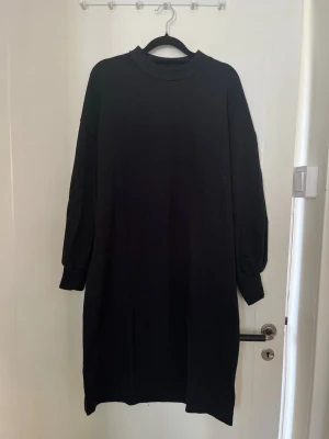 Svart långärmad sweatshirtklänning med hög krage - En enkel och stilren svart klänning med långärmade och hög krage. Klänningen har en rak och loose passform som ger en avslappnad look.