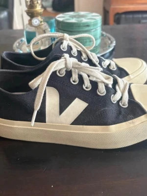 Svarta Veja sneakers med vit logga - Säljer ett svarta Veja sneakers med vit logga på sidan och vita snören. Sulan har gulnat (syns på sista bilden) annars i toppen skick! 