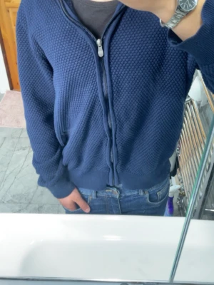 Blå ziptröja med strukturmönster - Snygg blå ziptröja med strukturmönster och ribbade muddar. Tröjan har dragkedja framtill och är tillverkad i ett mjukt material som känns skönt mot huden. Perfekt att slänga på sig när det är lite kyligt ute.