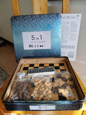 5 i 1 brädspelsset Collection Classique - Säljer ett 5 i 1 brädspelsset från Collection Classique med schack, dam, backgammon, domino och tärningar. Setet kommer i en blå metallask med geometriskt mönster och innehåller spelpjäser i trä och plast i bruna och beige nyanser samt ett spelbräde i trälook.