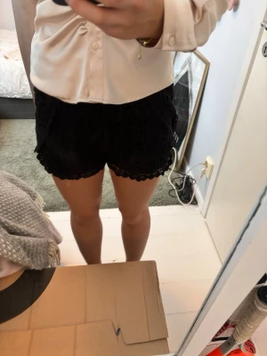 Svarta spetsade shorts - Säljer ett par snygga svarta shorts med spetsdetaljer och dekorativt mönster. De har en feminin look med scallop-kant och är perfekta för varma dagar. Passformen är normal och de är midwaist. Perfekt att matcha med en enkel topp.