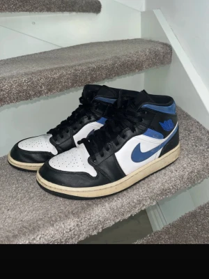 Nike Air Jordan 1 svart/blå/vit - Säljer ett par Nike Air Jordan 1 sneakers i svart, blått och vitt läder. Har en smutsig sula som enkelt går att rengöra, löser man det är den så gott som ny förutom undersidan på hälen som har ett litet hål.