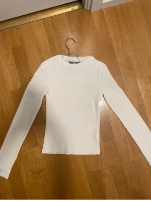 Vit långärmad ribbad topp från bikbok  - En enkel och stilren vit långärmad topp från bikbok. Toppen är ribbad och har en normal passform med rund halsringning. Perfekt att matcha med jeans eller kjol för en clean look.
