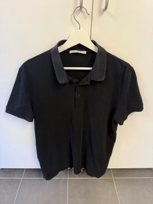 Svart piké från Tiger of Sweden stl L - Säljer en svart polotopp från Tiger of Sweden med klassisk krage och knappslå framtill. T-shirten har korta ärmar och är tillverkad i mjuk bomull. Perfekt för dig som gillar stilrena och tidlösa plagg.