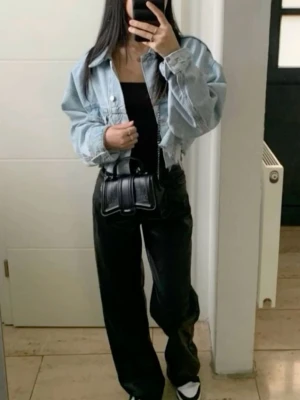 Ljusblå croppad jeansjacka - Trendig ljusblå croppad jeansjacka med råa kanter och klassisk krage. Jackan har knappstängning framtill och två bröstfickor. Perfekt för en avslappnad och cool stil.