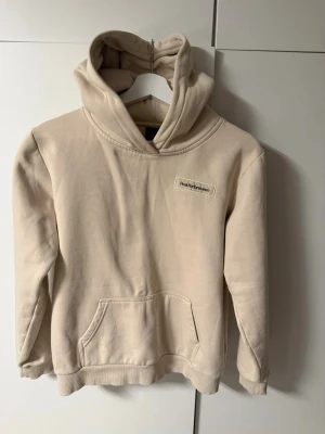 Beige hoodie från peak performance  - Säljer en beige hoodie från peak performance med huva och stor magficka. Hoodien har ett broderat märke på bröstet och är gjord i mjukt bomullsmaterial. Perfekt för dig som gillar en clean och enkel look.