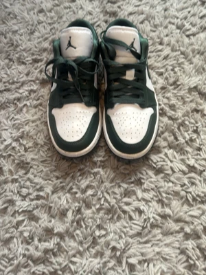 Air Jordan 1 Low vit och mörkgrön - Säljer ett par Air Jordan 1 Low sneakers i vitt och mörkgrönt läder. Dom är knappt använda så dom är i fint skick! Dom har även crease skydd i skon som hänger med. Dom är äkta!