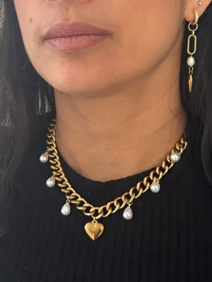 Guldpläterat halsband 9 mm med hjärthänge - Ett elegant och trendigt statement-halsband i varm guldig ton. Den kraftiga 9 mm kedjan kombineras med vackra droppformade pärlor och ett dekorativt hjärthänge som ger smycket en feminin och lyxig känsla. Perfekt både till vardag och fest.  Matchande örhängen finns att köpa separat för en komplett look. Finns även i silverfärgad variant.  Material: 18K guldplätering på rostfritt stål Bredd: 9 mm Längd: Justerbar 38–43 cm Egenskaper: Nickelfritt & handgj
