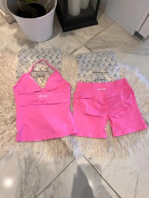 Blossom DFYNE - Snyggt rosa träningsset från DFYNE med ett linne med smala axelband och V-ringning samt matchande shorts med hög midja och scrunch-detalj bak. Materialet är stretchigt och passar perfekt för gym eller sport. Setet är tillverkat i ett mjukt och bekvämt tyg. Impact: 4.5