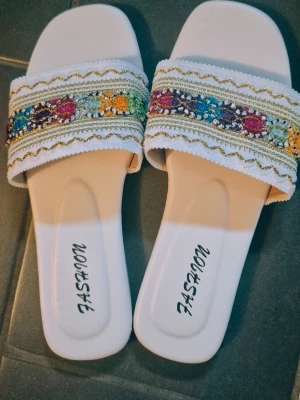 Fashion Slippers White Multicolored size 36 - Brand new never used  Indoor/outdoor, best for all A pair of slippers with a wide strap over the foot. The strap is decorated with a colorful pattern and golden details. The shoes have a flat sole and the text "FASHION" printed on the insole. Shipping same day if you order during opening hours of post office otherwise next day.