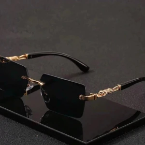 Svarta rektangulära solglasögon guld - Stilrena solglasögon med svarta, rektangulära glas och tunna guldfärgade detaljer på bågarna. Snygg minimalistisk design med svarta skalmar och exklusiv känsla. Perfekta för dig som vill ha en trendig accessoar med lyxig touch.