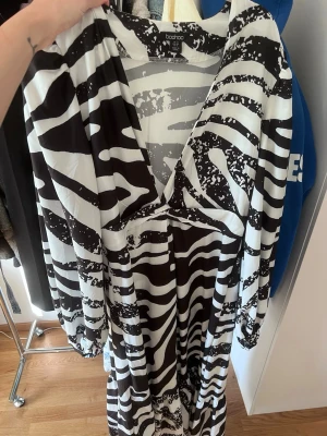 Zebramönstrad klänning Boohoo - Snygg zebramönstrad klänning från Boohoo i svart och vitt. Klänningen har lång ärm, djup v-ringning och ett knyt framtill. 