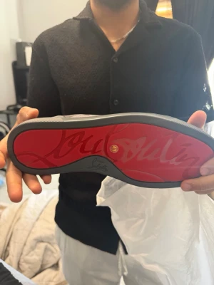 Grå sneakers  - Snygga grå sneakers med röd sula. Fick de i present men är för små. Skorna har en låg profil, rund tå och är tillverkade i ett mjukt material med matchande grå snörning. Perfekt för dig som vill sticka ut med exklusiva skor. Vet ej vart de är ifrån 