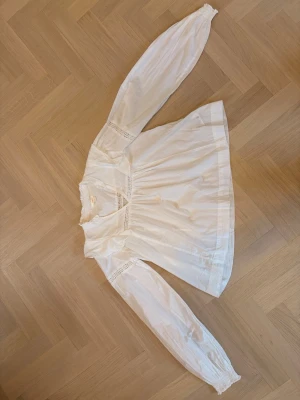 Vit blus med spetsdetaljer - Söt vit blus med lång ärm och fina spetsdetaljer vid axlar och bröst. Blusen har en lös passform, rundad halsringning och lätt puffade ärmar med resår vid ärmslut. Aldrig använd.