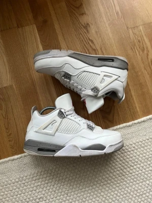Nike Air Jordan 4 White Oreo sneakers - Nike Air Jordan 4 White Oreo sneakers i vitt och grått med meshpaneler och detaljer i plast. Skorna har snörning, rund tå och en platt sula med grå stänkdetaljer. Klassisk siluett och ikoniska detaljer som synlig Air-enhet i sulan.