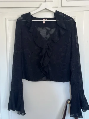 Svart volangblus från Nelly  - Snygg svart blus med volangkant längs urringningen och framtill. Aldrig använd, ny skick❣️