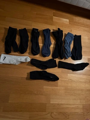 Mixade strumpor i svart, grått och vitt - Säljer ett blandat paket med strumpor i olika färger: svart, mörkgrå, ljusgrå och ett par vita med en svart siffra. Strumporna är i klassisk modell och passar perfekt till vardags. Materialet är främst bomull med inslag av syntet för extra komfort.