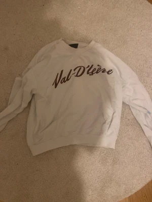 Vit sweatshirt med Val D'Isère-tryck - Vit sweatshirt med rund hals och brunt Val D'Isère-tryck på bröstet. Tröjan har en avslappnad passform och ribbade muddar vid ärmslut och nederkant. Perfekt för en chill och sportig look. Det finns några små fläckar på tröjan men det syns inte så bra. Står ej för frakt. Pris kan diskuteras 25-30kr