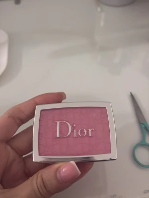 Dior rosa puderrouge - Säljer ett puderrouge från Dior i en intensiv rosa nyans. Rouget kommer i en elegant silverfärgad dosa med spegel och har ett pressat mönster med Dior-loggan på ytan. Perfekt för att ge kinderna en fräsch och ungdomlig look.