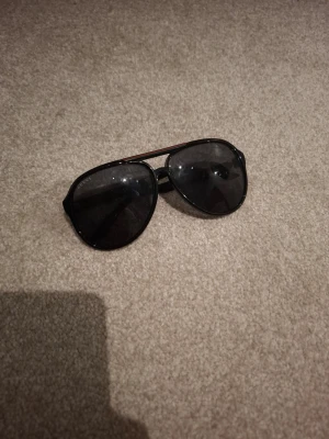 Svarta aviator solglasögon från Gucci - Snygga svarta aviator solglasögon från Gucci med mörka glas och klassisk metallbåge. Diskret Gucci-logga på sidan och stilren design som ger en cool vibe. Perfekta för att lyfta din look under soliga dagar. Fodral tillkommer men det sitter oeehört löst. Nypris på dessa brukar ligga på 2000 och uppåt. 
