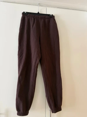 Bruna mjukisbyxor med resår - Mörkbruna mjukisbyxor med resår i midjan och vid bensluten. Tillverkade i mjukt bomullsliknande material som känns skönt mot huden. Byxorna har en avslappnad passform och är perfekta för chill dagar hemma eller när du vill vara bekväm.