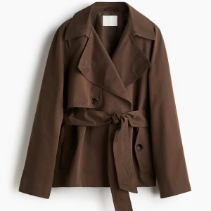 Brun trenchcoat med knytskärp från H&M - Stilren brun trenchcoat med bred krage och knytskärp i midjan. Jackan har dubbelknäppning framtill, långa ärmar och två sidofickor. Tillverkad i ett kraftigt tyg som ger en snygg siluett. Perfekt för dig som gillar klassisk men trendig stil. Storlek S, använt ungefär 3-4 gånger. 