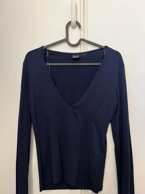 Mörkblå v-ringad topp Gina Tricot - Mörkblå långärmad topp från Gina Tricot med v-ringning och figurnära passform. Tillverkad i mjukt material. Tröjan har även hål för tummarna. 