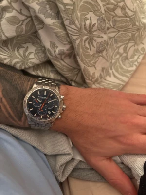 Raymond Weil Tango kronograf - Raymond Weil Tango 300 med blå urtavla och referensnummer 8560-ST2-50001 (eller liknande regionala varianter som 8560-ST2-20001).  Viktiga funktioner  Märke och kollektion: Raymond Weil, Tango-kollektionen.  Urverk: Schweiziskt kvartskronografurverk.  Material i boett och armband: Rostfritt stål.  Urtavlans färg: Blå, med index och självlysande visare.  Vattentålighet: Dykarklassning på 300 meter (1000 fot), lämplig för blandad dykning.  Funktioner: Kronograf (stoppur), datumvisning mellan klock