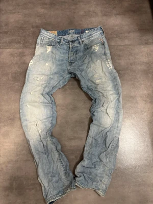 Ljusblå slitna jeans från Replay - Säljer ett par ljusblå jeans från Replay med distressed detaljer och slitningar på både fram- och baksida. Jeansen har klassisk femficksmodell, raka ben och är tillverkade i denim. Perfekta för en avslappnad och trendig look.