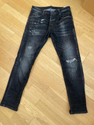 Svara dsquared2 jeans - Svarta jeans| bra skick förutom att loggan där fram är borta som man ser på bilden, det är även en söm som är borta på märket därbakom och det ser man också på bild, därav pris. Annars prima| runt 100cm långa och dom passar mig, jag är runt 184-186cm