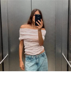Ljusrosa offshoulder topp - Trendig ljusrosa offshoulder topp med skrynklig struktur och croppad passform. Toppen är ärmlös och har en snygg, figurnära siluett som passar perfekt till jeans eller kjol. Perfekt för dig som vill ha en söt och modern look.